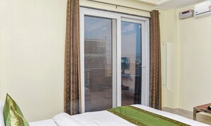 A hotel room with a bed, a window with curtains, and an air conditioning unit on the wall.
