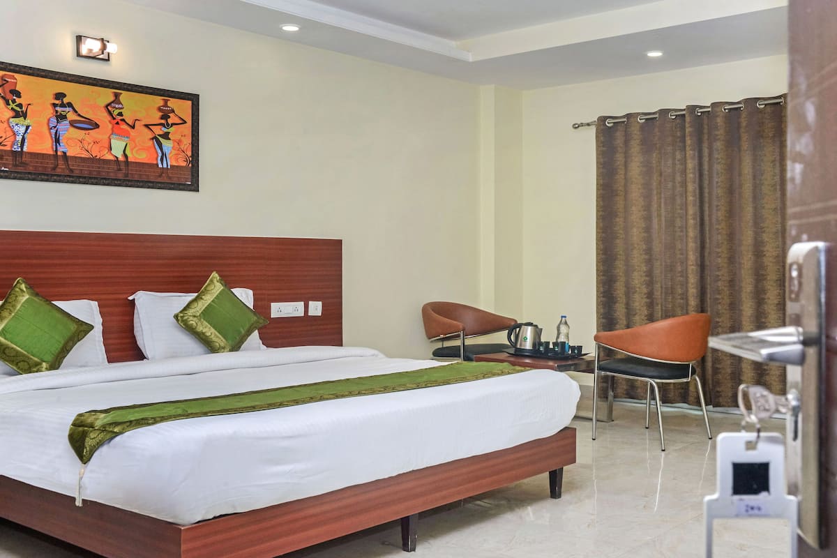 A hotel room with a bed, a chair, a table, and a painting on the wall.