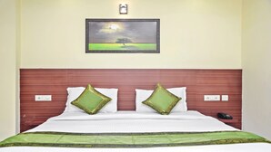 A neatly made bed with a green and white bedspread, two decorative pillows, a framed landscape painting above the bed, and a bedside telephone. - Treebo Trip Vikrant's Residency (Gurugram)