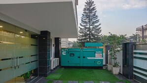 A courtyard with a green lawn, a tall tree, and a green generator labeled 'suhir'. - Treebo Trip Vikrant's Residency (Gurugram)