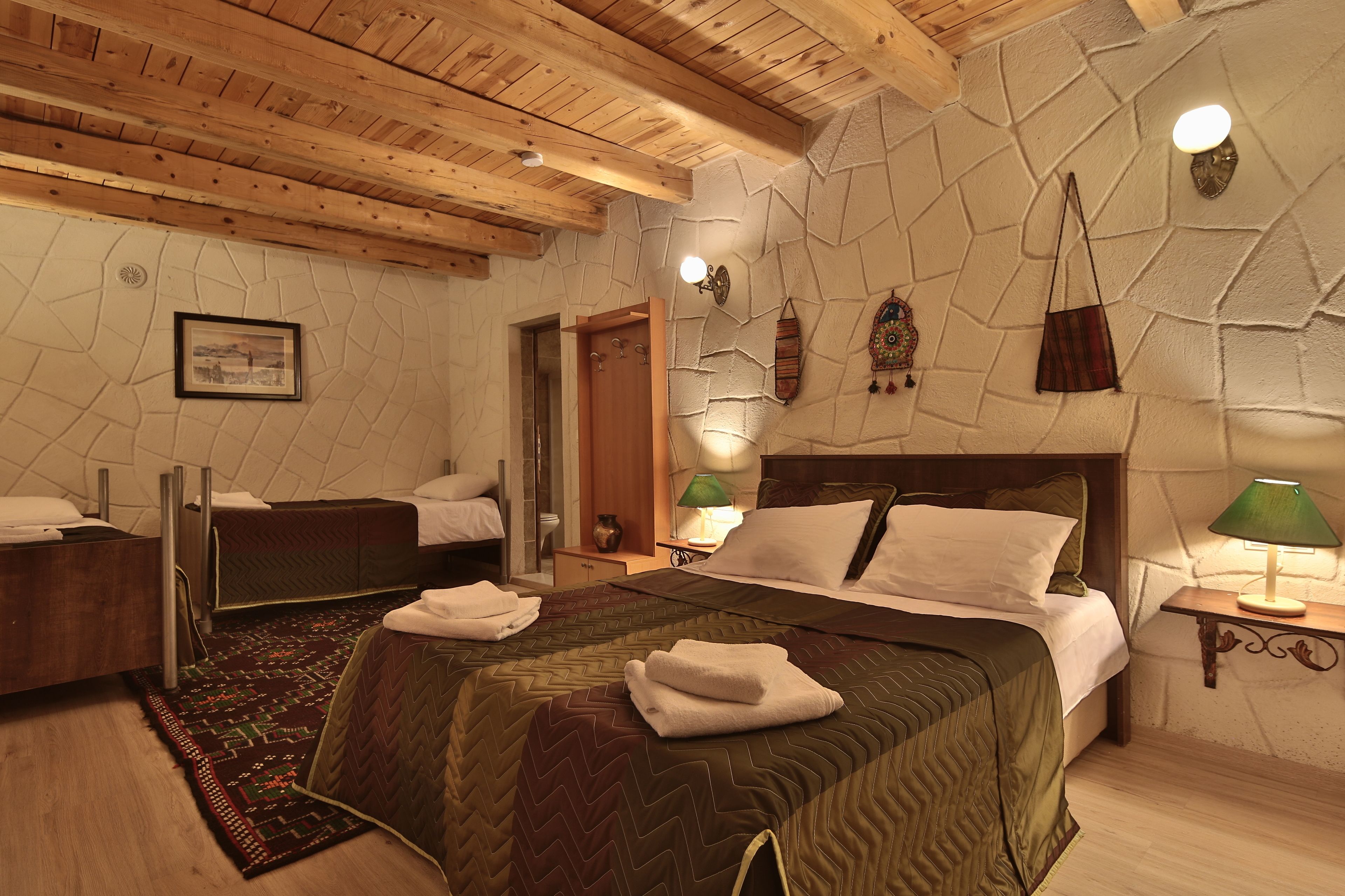 Una habitación con una cama, mesitas de noche, un espejo, una lámpara de pared y una puerta.