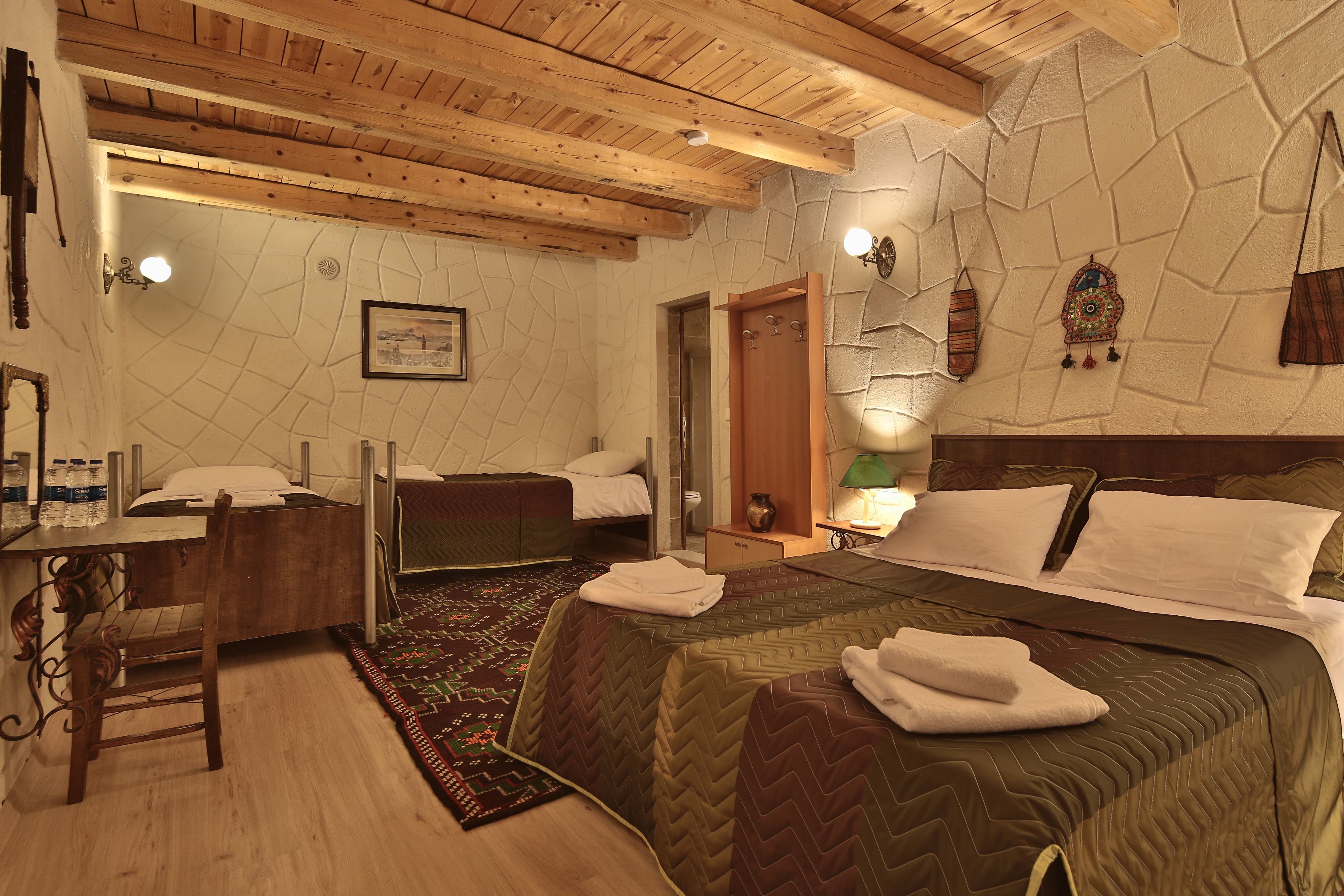 Un dormitorio con techo de madera, una cama con colcha, un escritorio con silla y una mesita de noche con lámpara.