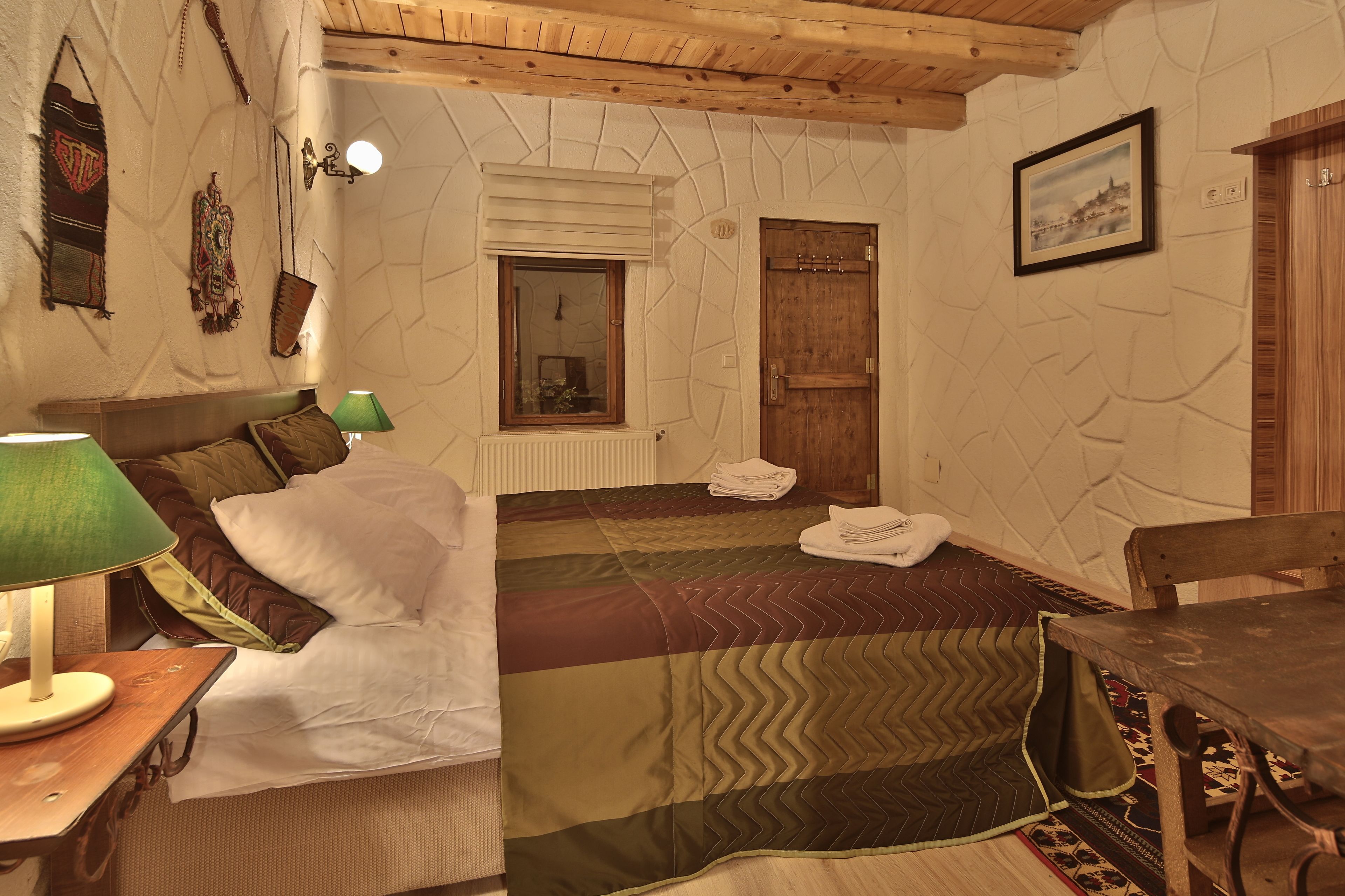 Ein gemütliches Zimmer mit einem Bett, einem Holzsessel, einem Tisch mit Lampe, einem Fenster und einer Tür.