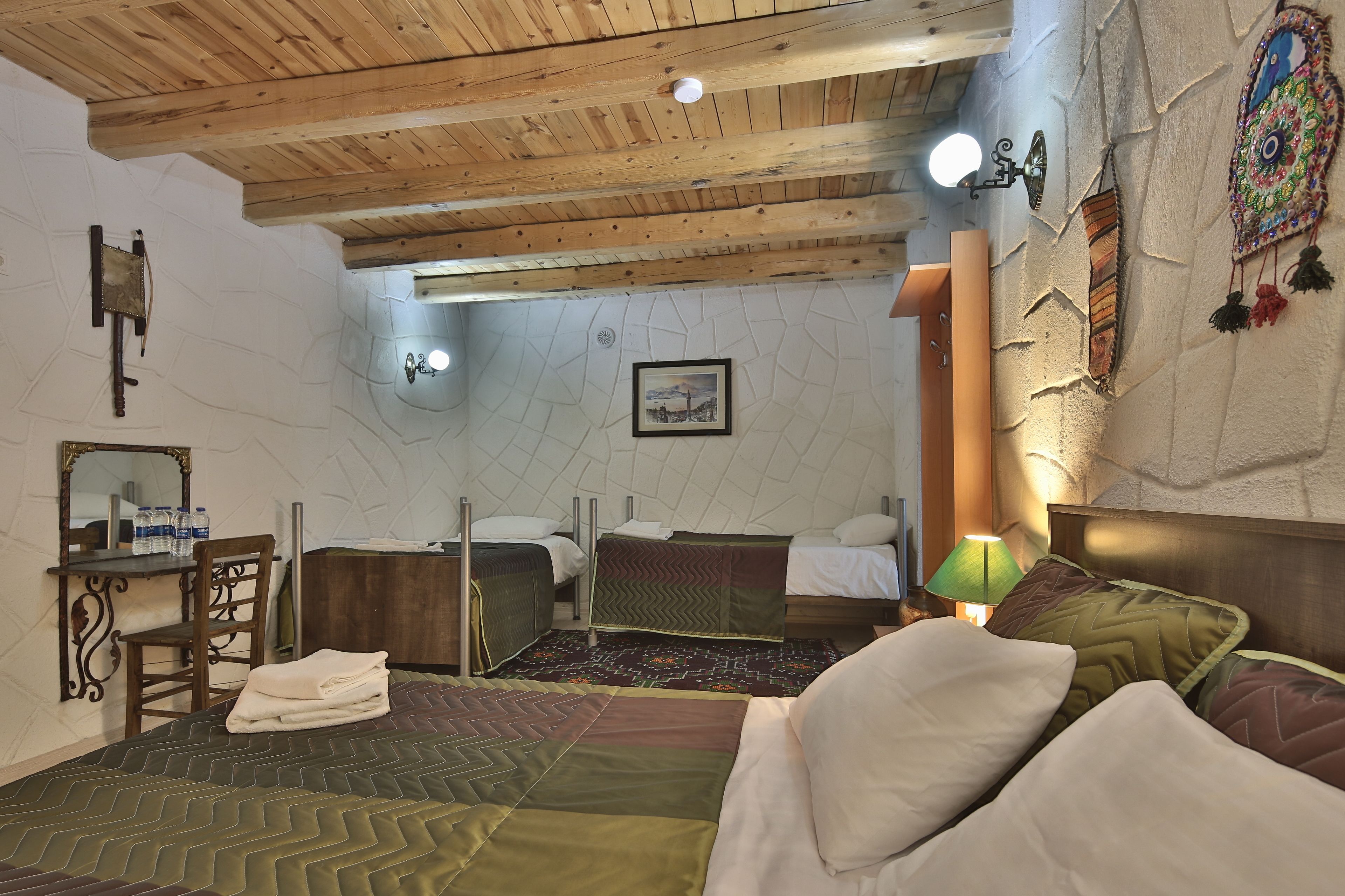 A bedroom with two beds, a desk with a chair, a mirror, and a wall-mounted lamp.