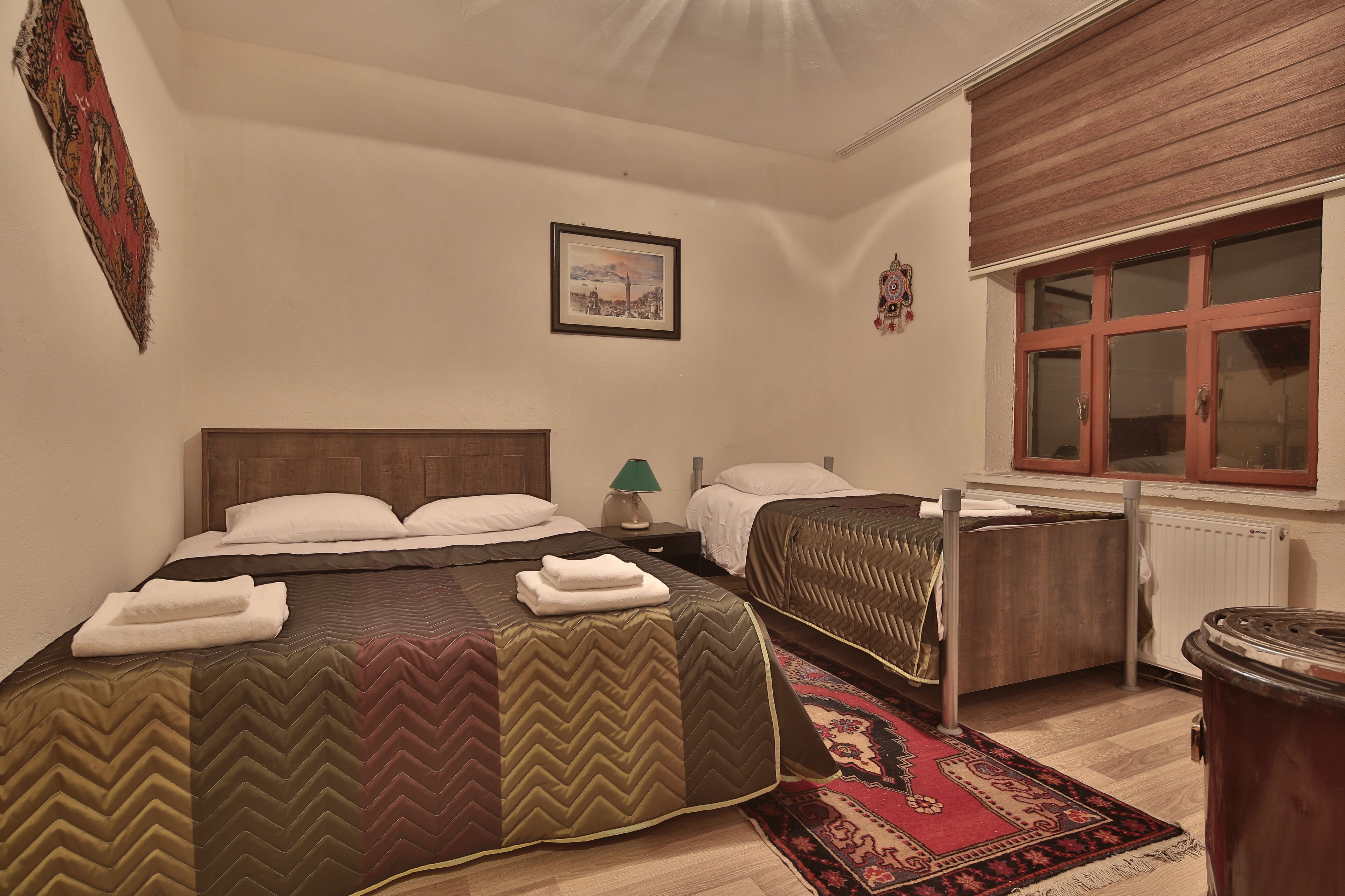 A bedroom with two beds, a wooden headboard, a radiator, a window with wooden shutters, and a framed picture on the wall.