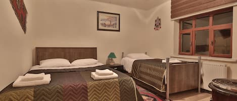 A bedroom with two beds, a wooden headboard, a radiator, a window with wooden shutters, and a framed picture on the wall.