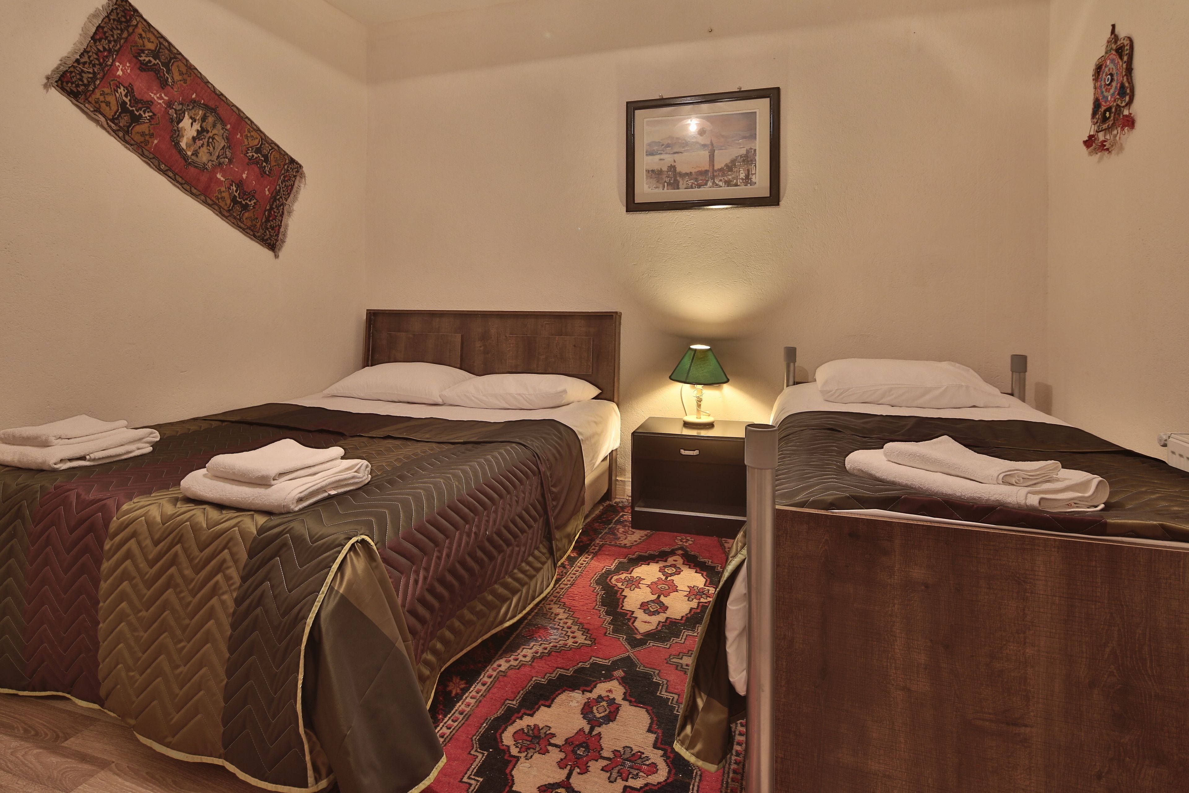 A hotel room with two beds, a nightstand, a lamp, and a decorative rug.