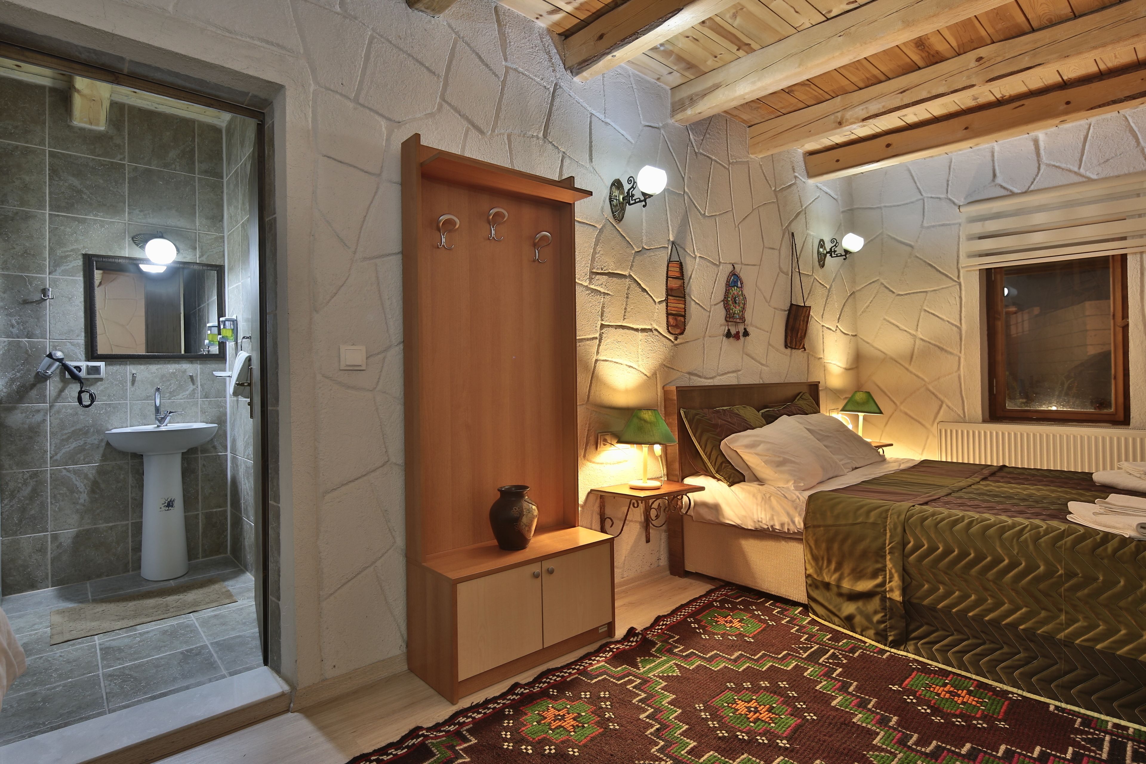Un dormitorio con cama, mesita de noche con lámpara, armario de madera, espejo y baño con lavabo y ducha.