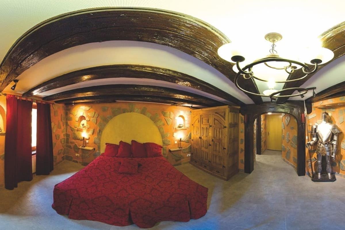 Una habitación con una cama grande, paredes de piedra, chimenea y televisión.