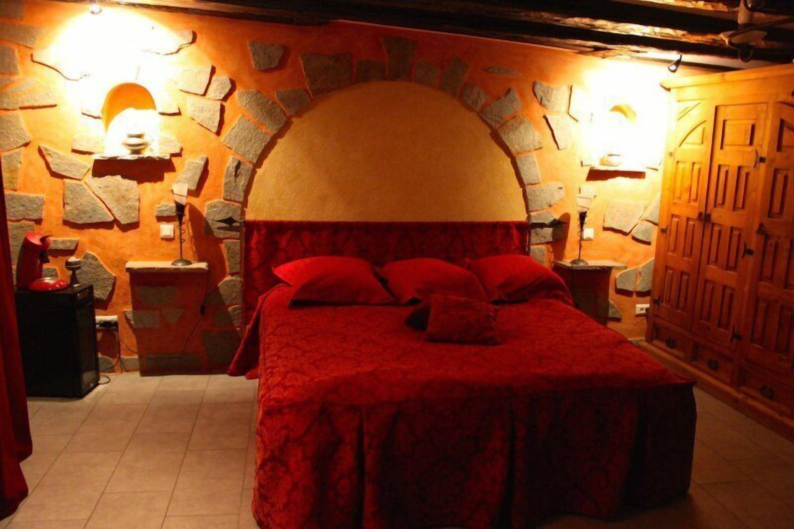 A bedroom with a stone arch ceiling, a red bedspread, and wooden furniture.