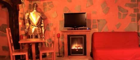 A room with a stone wall, a fireplace, a television, a red sofa, and a knight statue.