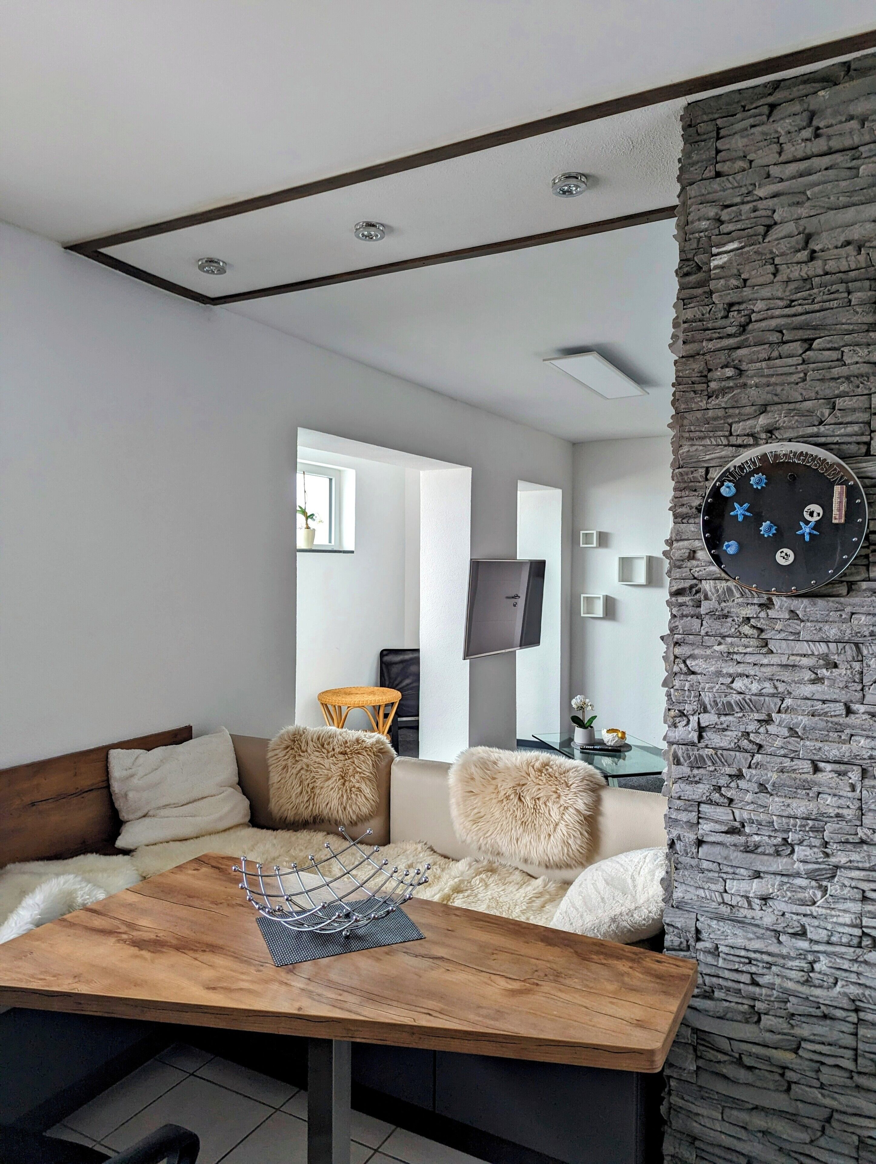 A modern living room with a stone accent wall, a wooden coffee table, and a sofa with fluffy cushions.