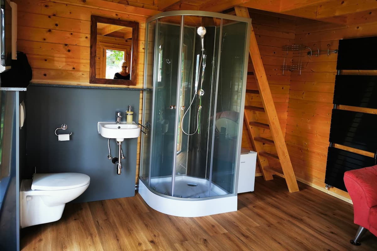 Baño de cabaña de madera con inodoro, lavamanos y ducha envuelta en vidrio.