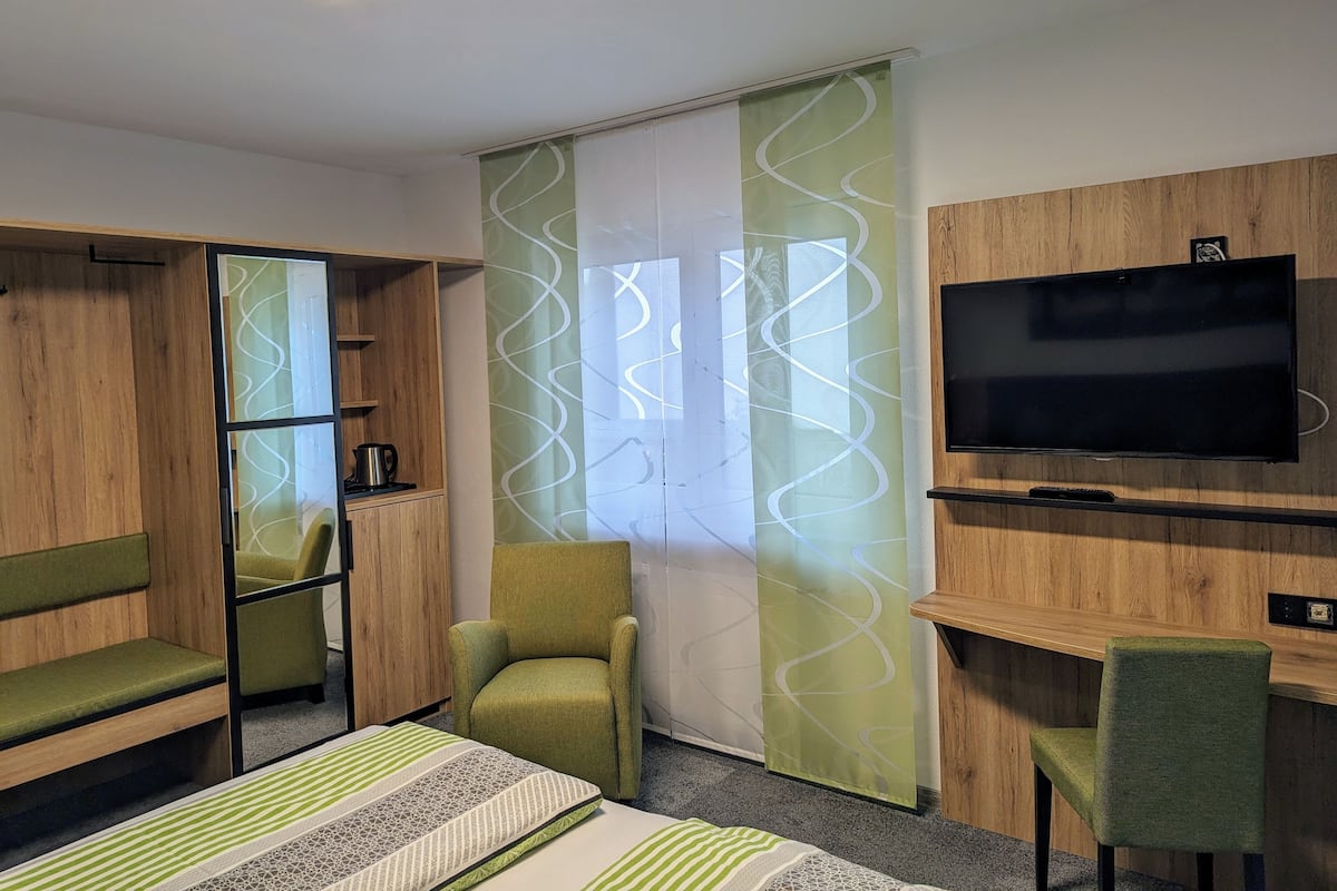 Una habitación con cama, televisión, sillón, escritorio y armario.