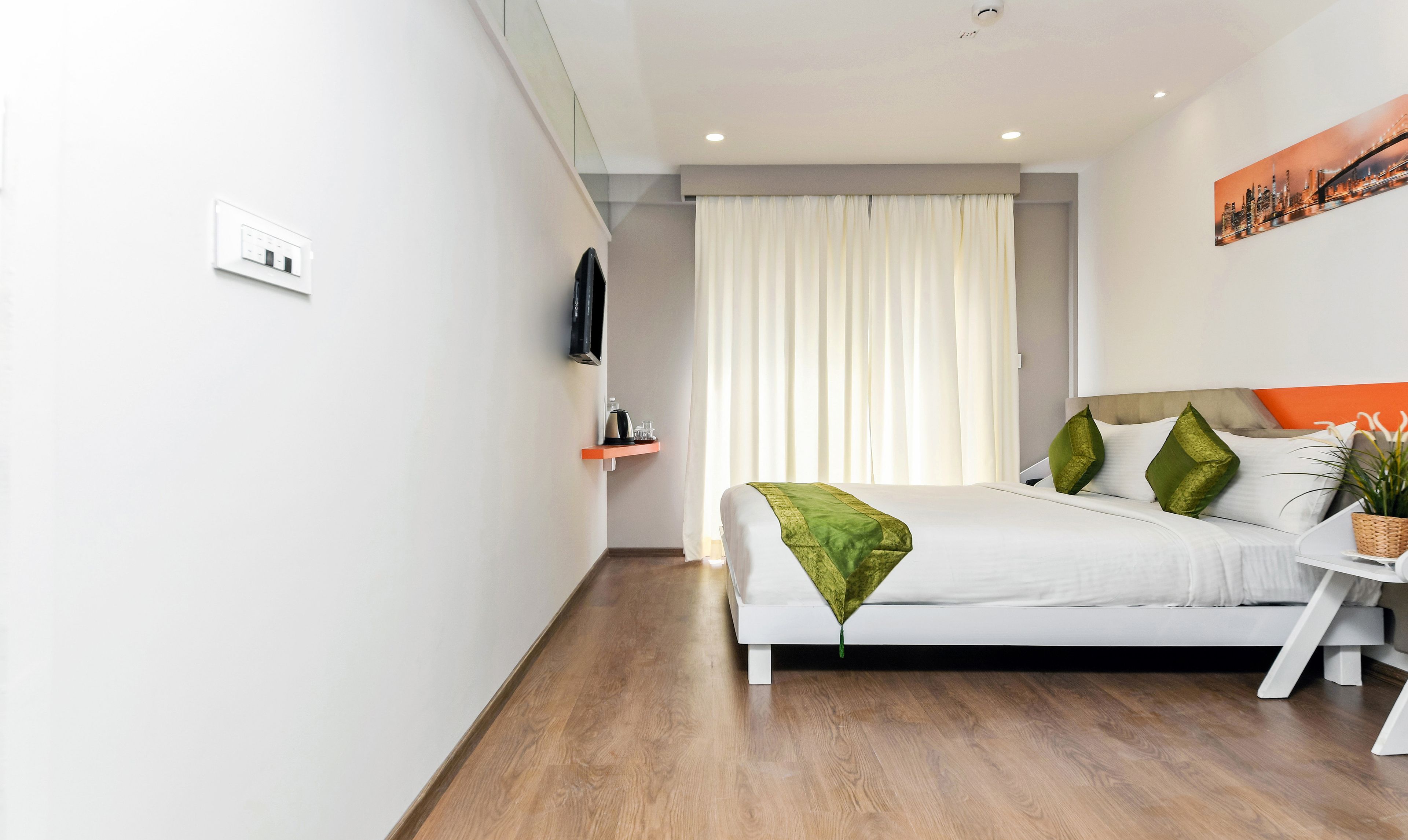 Una habitación de hotel moderna con una cama, un televisor, un pequeño estante con un hervidor y un cuadro en la pared.
