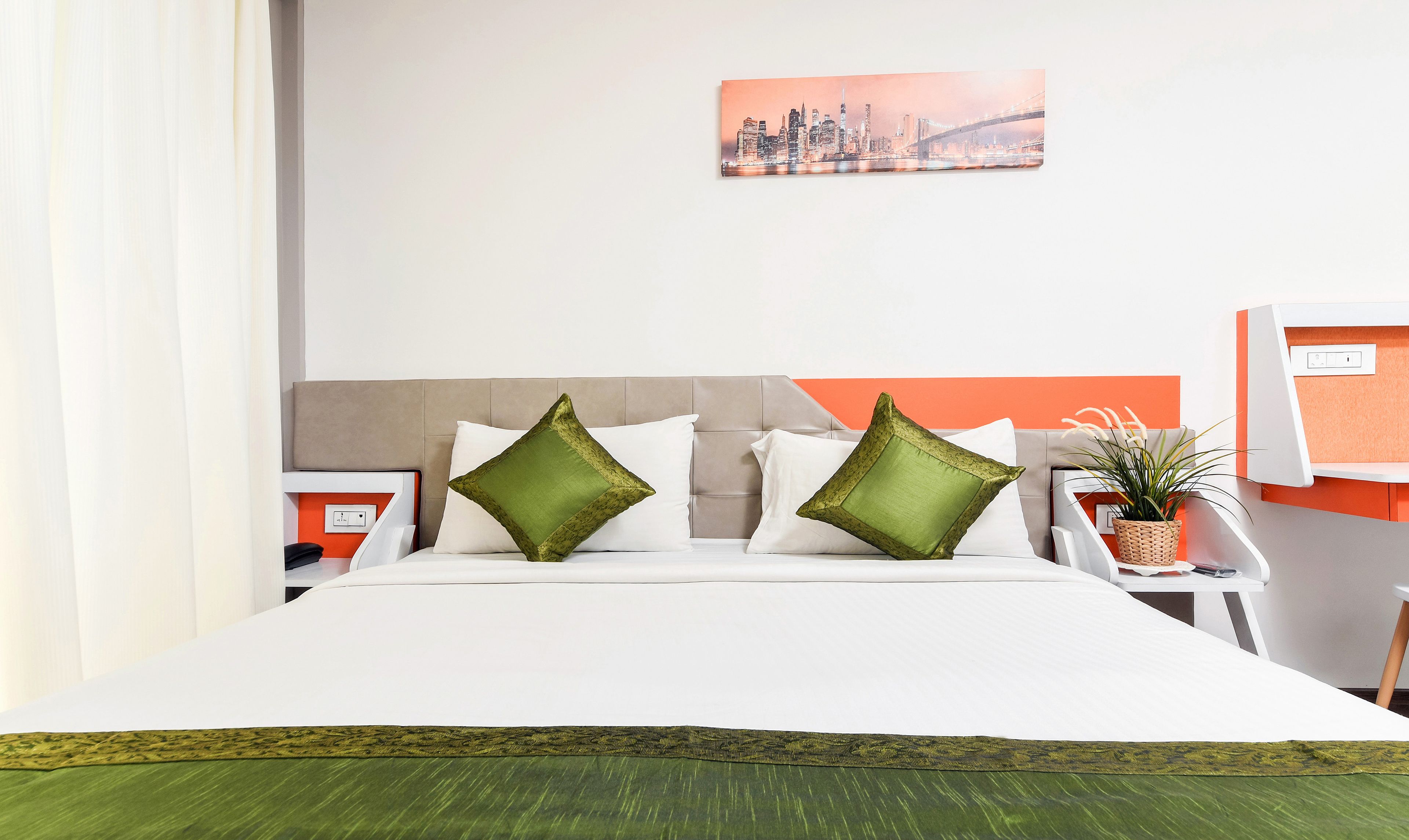 A hotel room with a bed, a nightstand, a desk, and a cityscape painting on the wall.