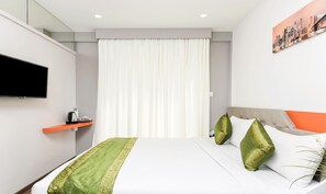 Una habitación de hotel moderna con una cama, un televisor de pantalla plana, una mesita de noche con una tetera y un cuadro de un paisaje urbano en la pared.