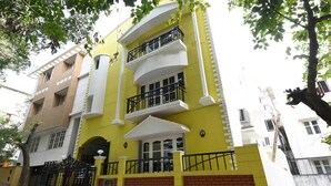 A multi-story yellow building with balconies, a gated entrance, and a brick base. - Itsy Hotels Shivas Kuteera (Bengaluru)