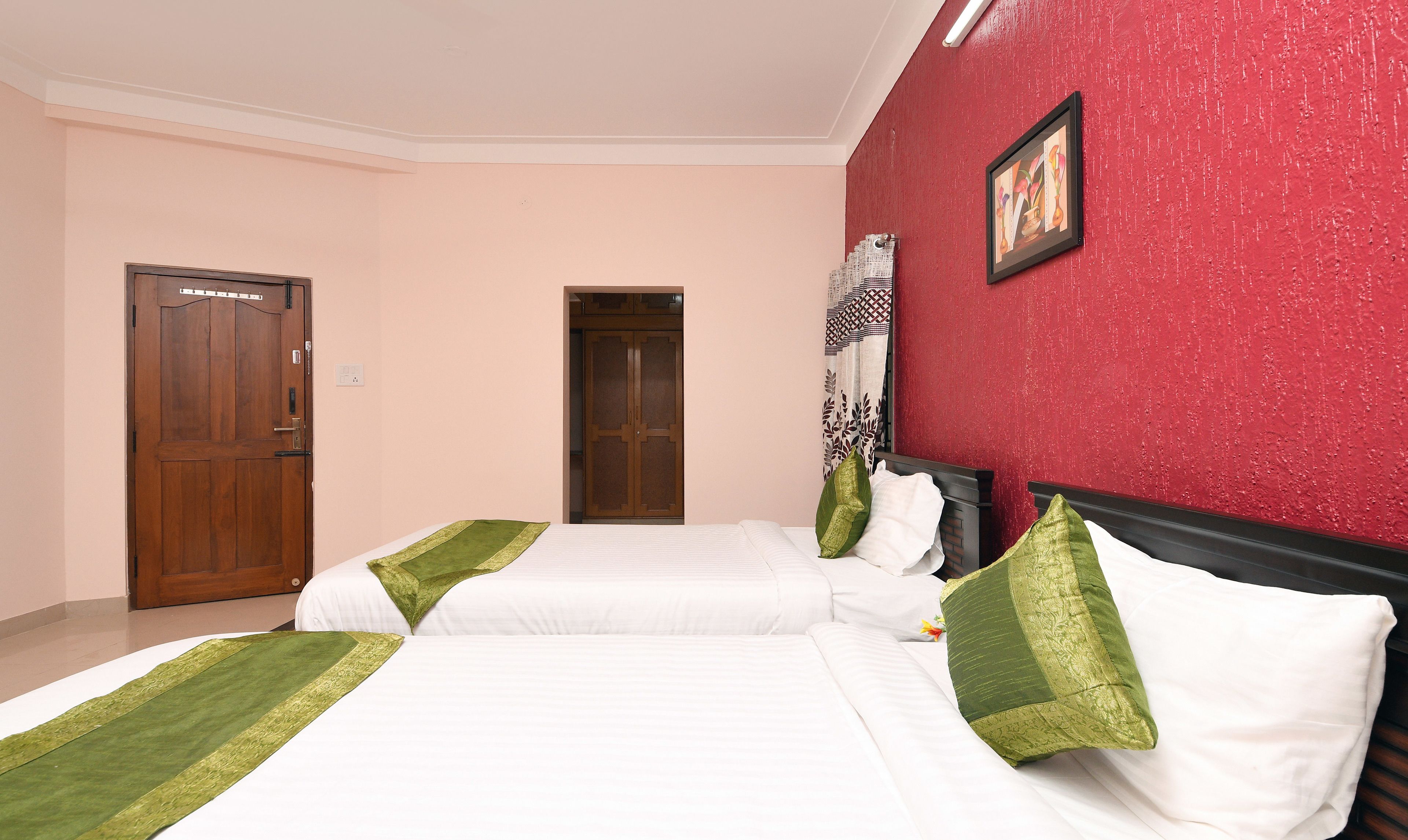 A hotel room with two beds, a red accent wall, a wooden wardrobe, and a door.