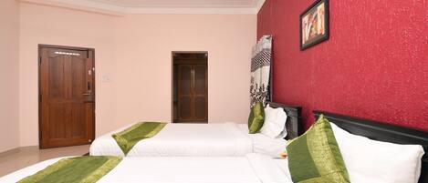 A hotel room with two beds, a red accent wall, a wooden wardrobe, and a door.