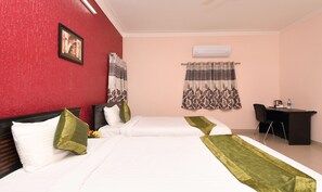 Two single beds with white linens and green throw pillows, a desk with a chair, and a coffee maker.