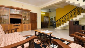 A living room with a sofa, coffee table, and TV stand. There is a staircase with a railing leading to another room. - Itsy Hotels Shivas Kuteera (Bengaluru)