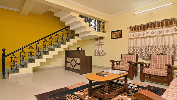 A living room with a staircase, wooden furniture, and a patterned rug. - Itsy Hotels Shivas Kuteera (Bengaluru)