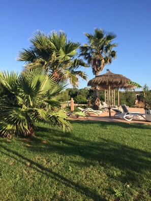 A garden with palm trees, a thatched-roof gazebo, and white lounge chairs. - Agroturismo Fincahotel Son Pou AG/322 (Felanitx)