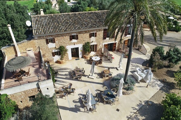 Un edificio de piedra con techo de tejas, zona de estar al aire libre y palmeras.