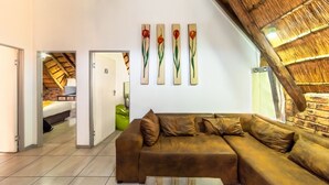 Una sala de estar moderna con un sofá seccional marrón, una mesa de centro de vidrio y un techo de paja. Hay cuatro paneles de madera con diseños florales en la pared.