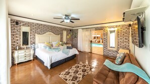 Un dormitorio con pared de ladrillo, cama con cabecera blanca, ventilador de techo, espejo grande y vista a una piscina a través de una puerta de vidrio.