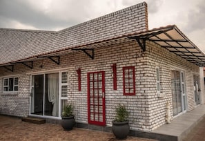 Un edificio con fachada de ladrillo, ventanas grandes con marcos rojos y un acceso cubierto.