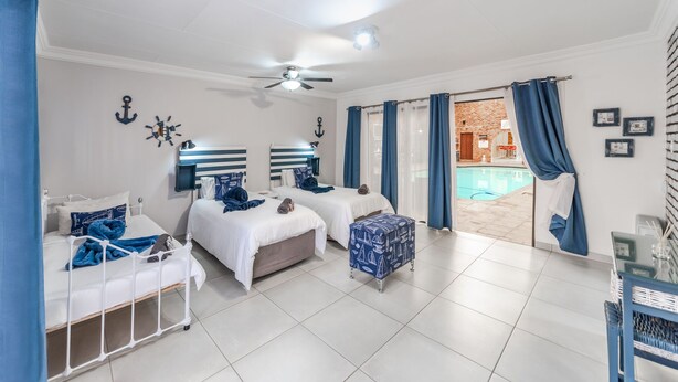 Habitación de hotel con dos camas, ventilador de techo, vista a una piscina exterior y una pared de ladrillo visible a través de la ventana.
