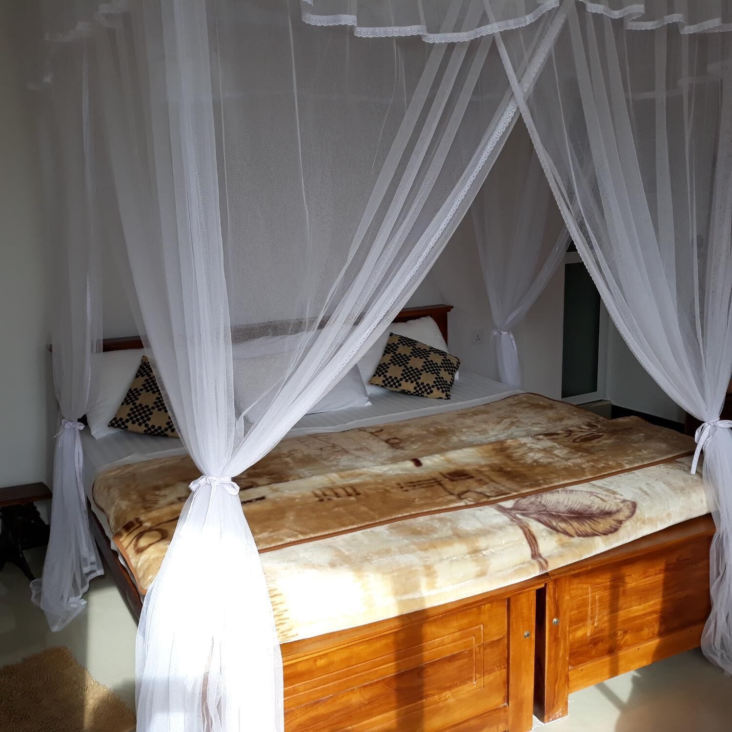 Una cama con estructura de madera y colcha estampada, cubierta por un dosel blanco.