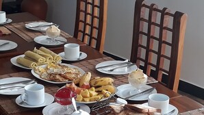 A dining table set with plates, cutlery, and various breakfast items like toast, fruit, and a dessert. - Lilly Guest Inn (Haputhale)