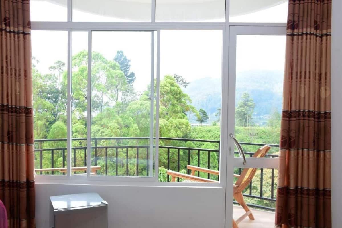 A room with a large window offering a view of a balcony with wooden furniture and a railing.