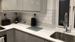 A modern kitchen with white cabinets, a stainless steel sink, and a window with a view of the sky. - Catherines Court (Solihull)