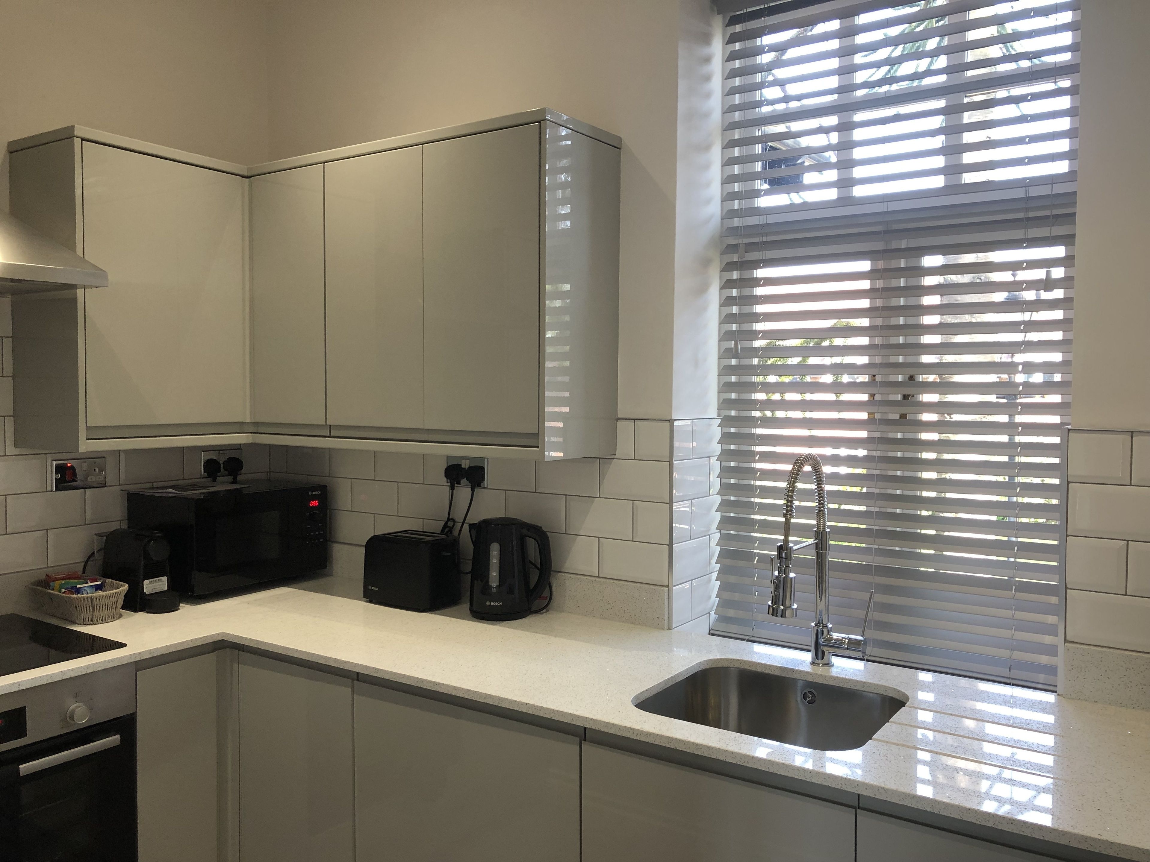Una cocina moderna con gabinetes blancos, un lavamanos de acero inoxidable, una cafetera Bosch y un tostador.