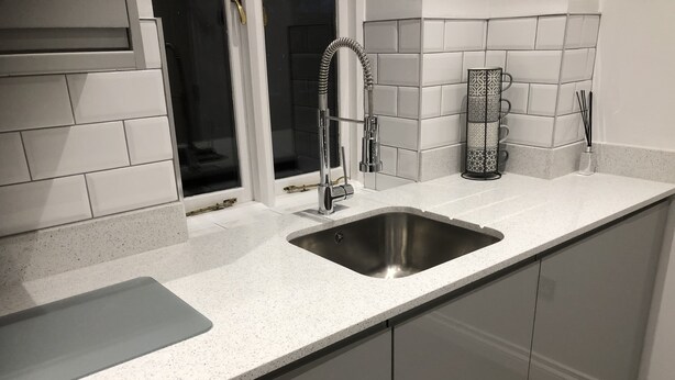 A kitchen with a stainless steel sink, a window, and a backsplash. - Catherines Court (Solihull)