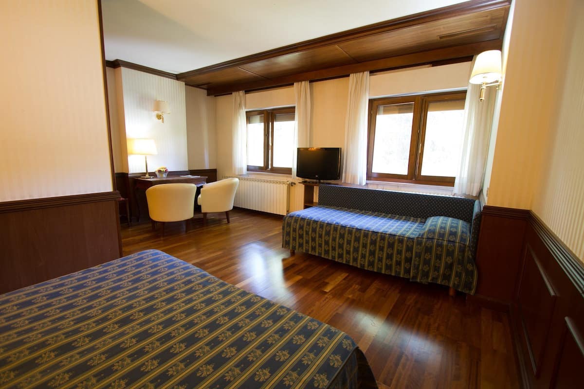 Habitación de hotel con dos camas, un escritorio, un televisor y ventanas amplias.