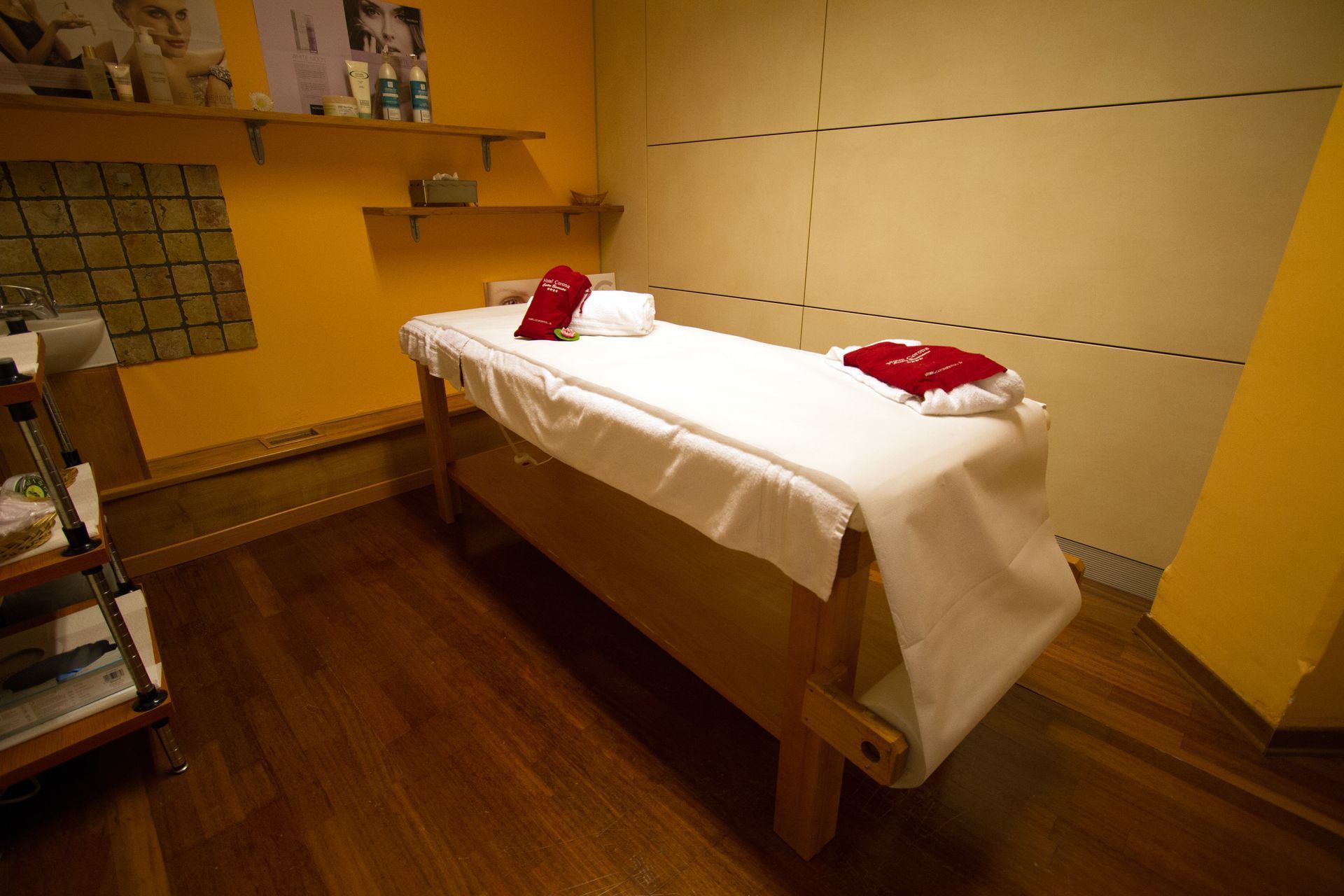 Una cama individual con sábana blanca y dos almohadas rojas en una habitación con suelo de madera y paredes amarillas.
