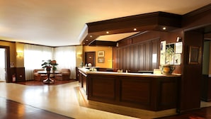 A hotel lobby with a reception desk, seating area, and a large wooden cabinet. - Hotel Corona (Pescasseroli)