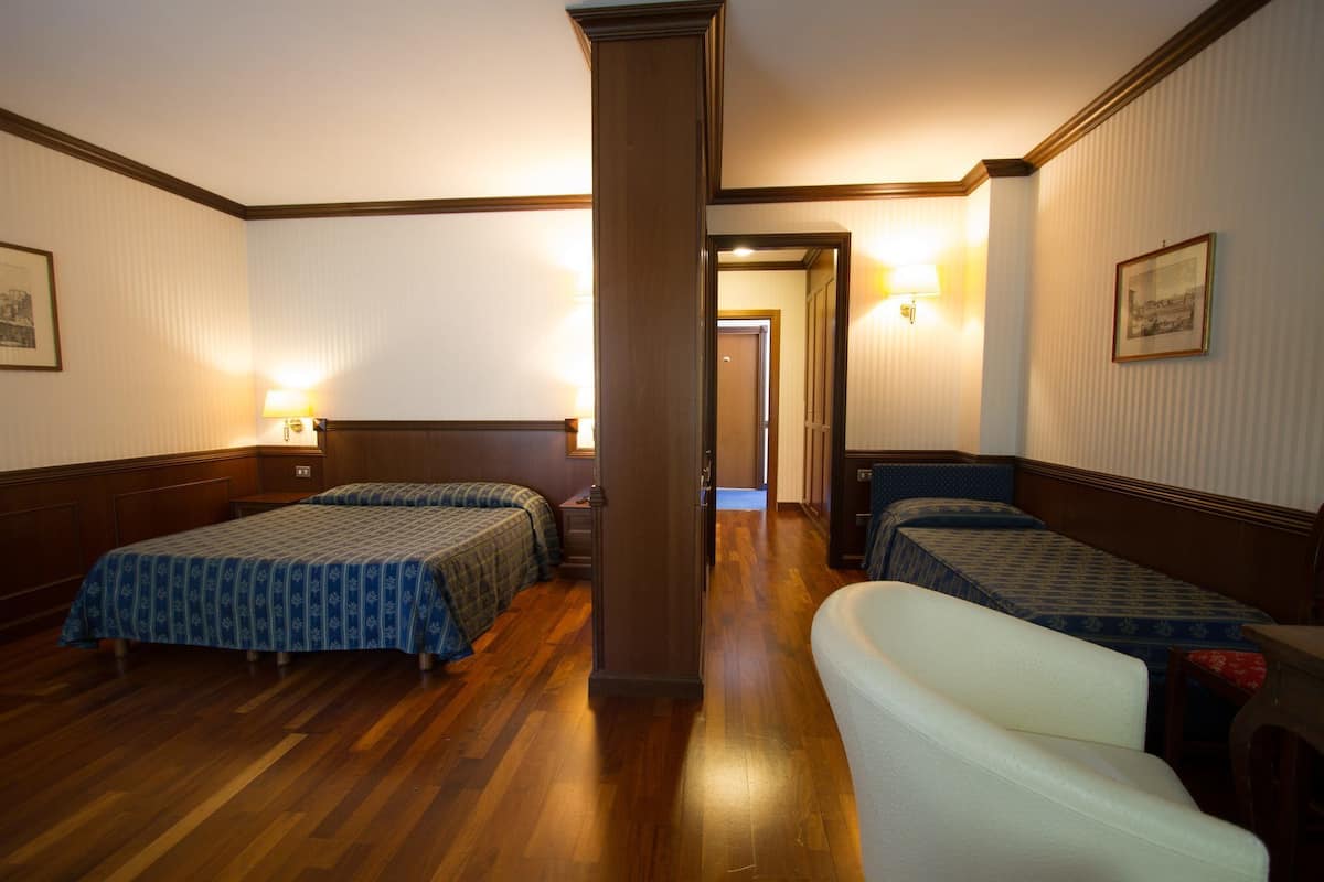 Una habitación de hotel con dos camas, una zona de estar y un pasillo que conduce a otra habitación.