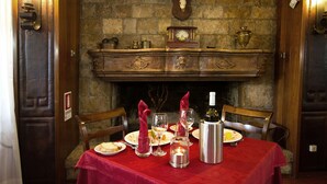 A dining table set with plates, glasses, and a wine bottle, with a fireplace and decorative items in the background. - Hotel Corona (Pescasseroli)
