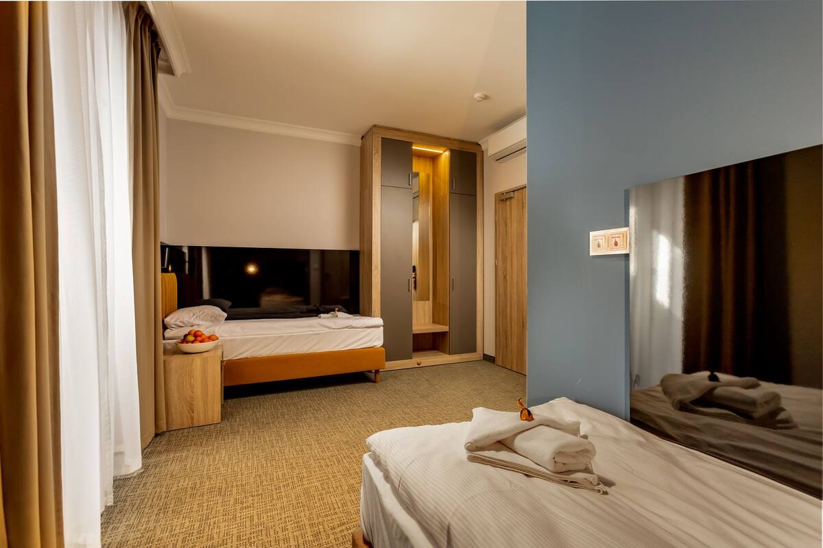 Habitación de hotel con dos camas, un espejo grande, una mesita de noche con un frutero y un aire acondicionado de pared.