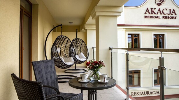 A balcony with wicker chairs, a table with a vase of flowers, and a sign for Akacja Medical Resort. - Akacja Medical Resort (Ciechocinek)