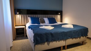A neatly made bed with blue and white bedding, a headboard, and a nightstand with a lamp. - Akacja Medical Resort (Ciechocinek)