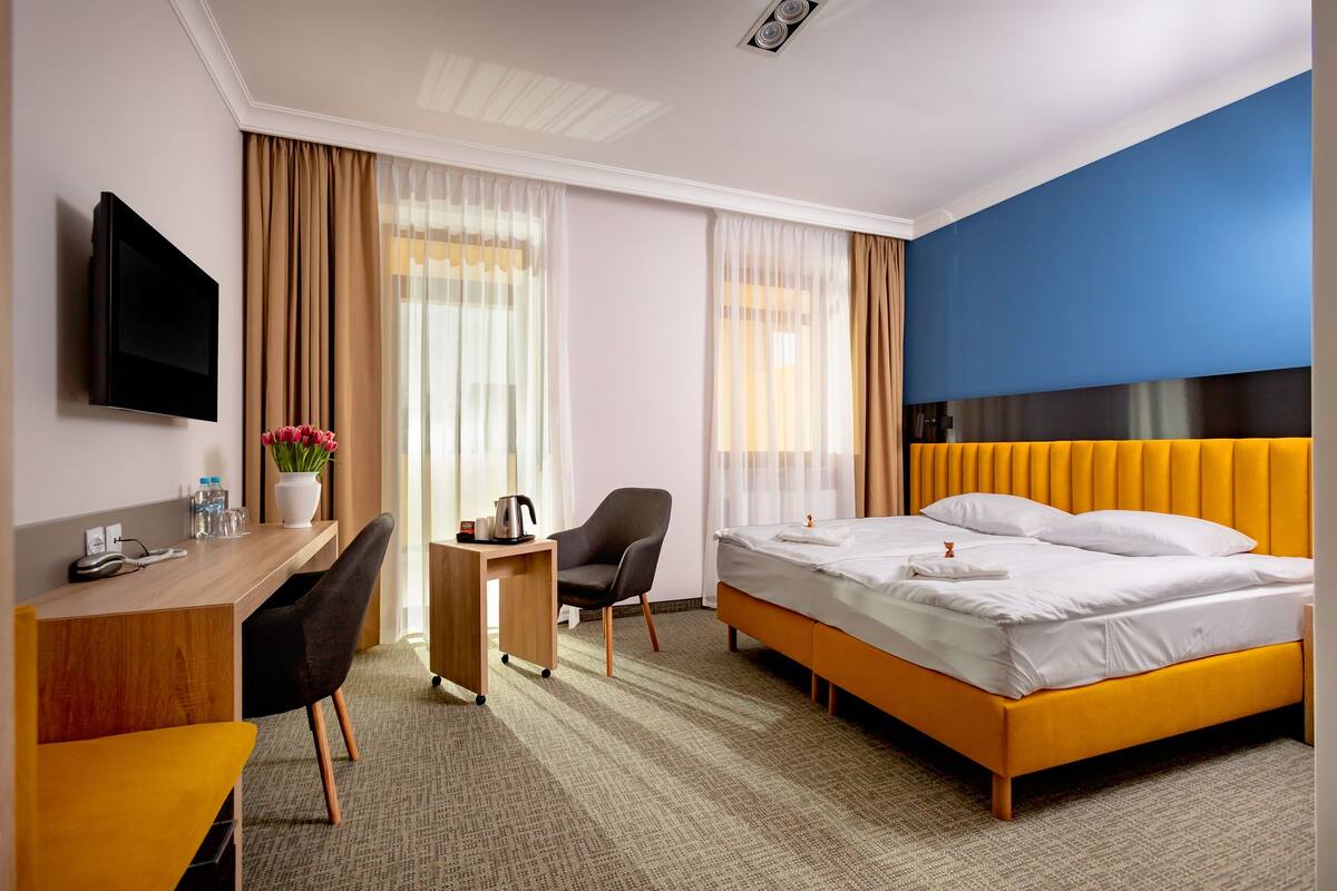 Habitación de hotel con cama, escritorio con silla, televisión y ventana con cortinas.