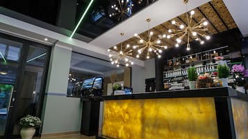 A modern bar area with a central counter, decorative ceiling lights, and a variety of bottles and plants on shelves.