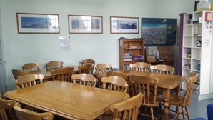 Un coin repas avec des tables et des chaises en bois, une bibliothèque et des tableaux encadrés accrochés au mur.